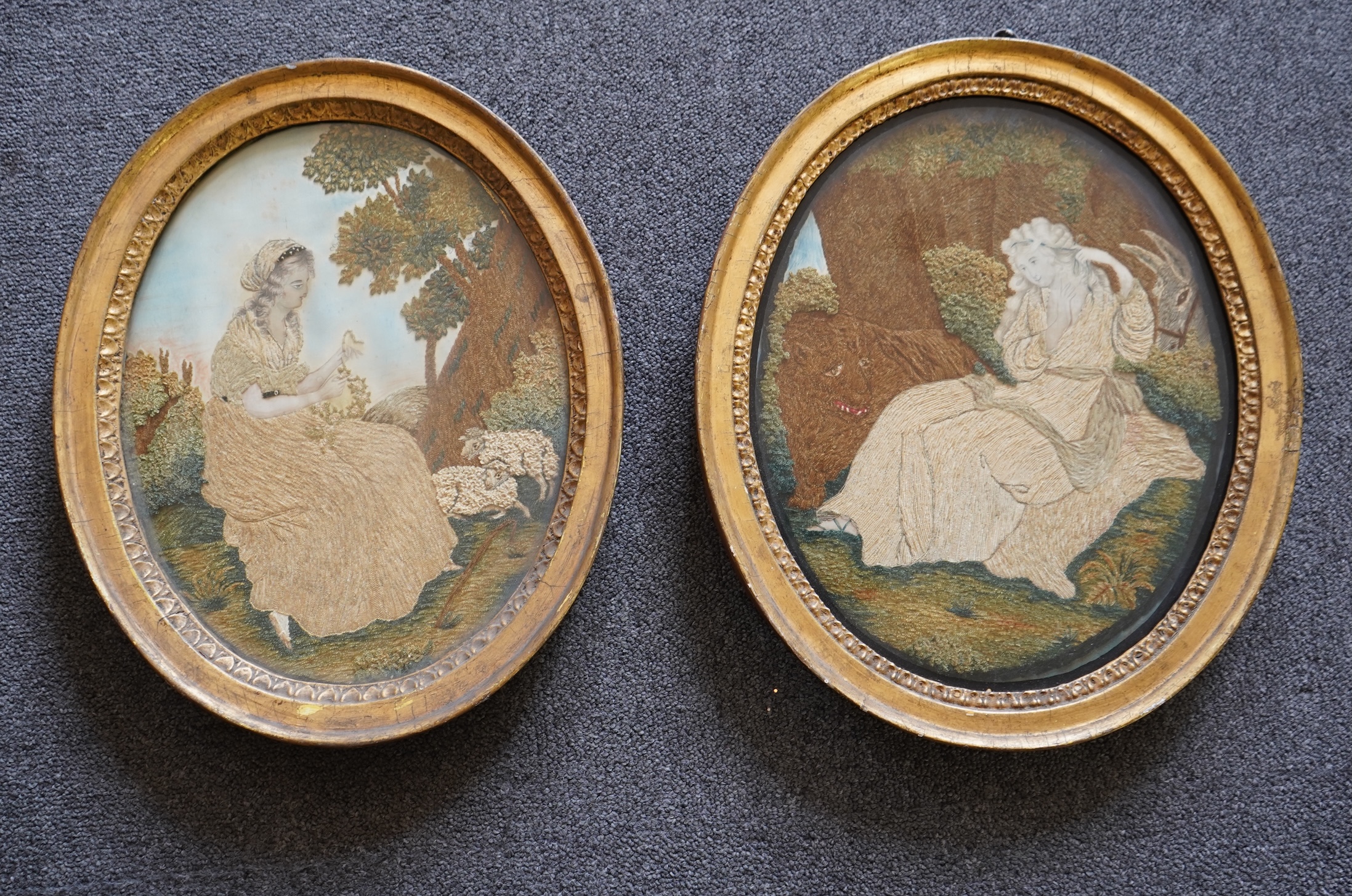 A pair of unusual early 19th century oval silk Chenille embroideries, one depicting a seated lady surrounded by a lion and donkey, the other depicting a seated shepherdess under tree with two sheep. Both have water colou